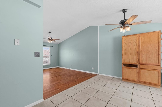 spare room with light wood-type flooring, vaulted ceiling, baseboards, and ceiling fan