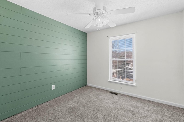 carpeted empty room featuring visible vents, ceiling fan, wooden walls, a textured ceiling, and baseboards