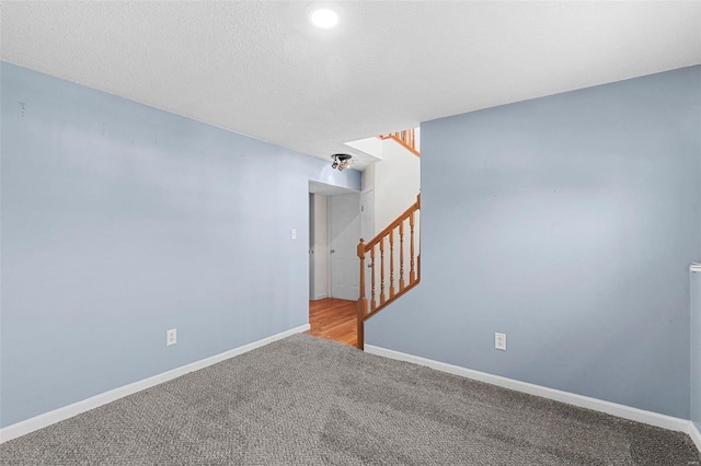 spare room featuring stairs, baseboards, a textured ceiling, and light colored carpet