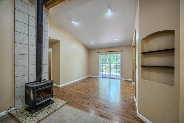 unfurnished living room featuring hardwood / wood-style floors, built in shelves, a wood stove, and vaulted ceiling with beams