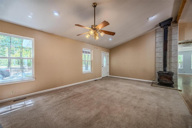 unfurnished living room with lofted ceiling, plenty of natural light, a wood stove, and carpet flooring