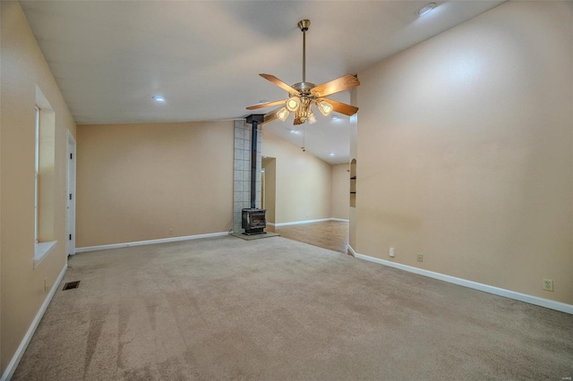 unfurnished room featuring ceiling fan, a wood stove, light carpet, and vaulted ceiling