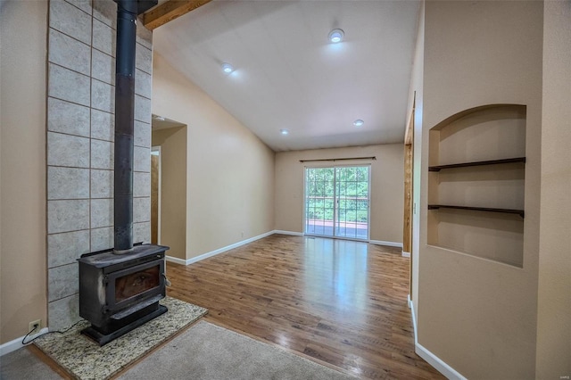 unfurnished living room featuring a wood stove, vaulted ceiling with beams, hardwood / wood-style floors, and built in features