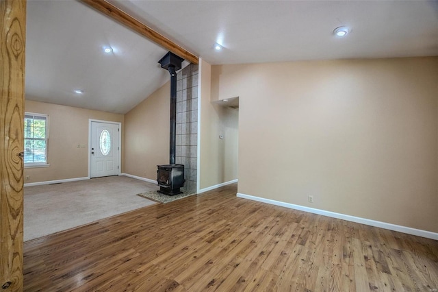 unfurnished living room with lofted ceiling with beams, a wood stove, and carpet flooring