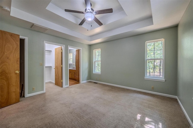 unfurnished bedroom with ensuite bath, light carpet, and a tray ceiling