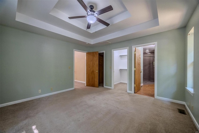 unfurnished bedroom featuring a walk in closet, a tray ceiling, light carpet, and ceiling fan