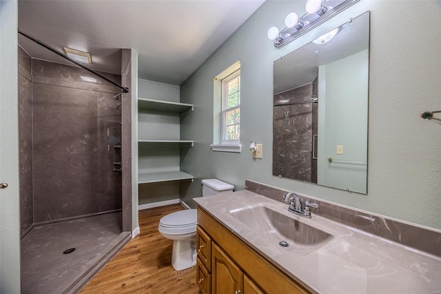 bathroom with toilet, hardwood / wood-style flooring, a tile shower, and vanity