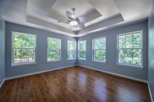 spare room with a textured ceiling, dark wood-type flooring, ceiling fan, and a raised ceiling