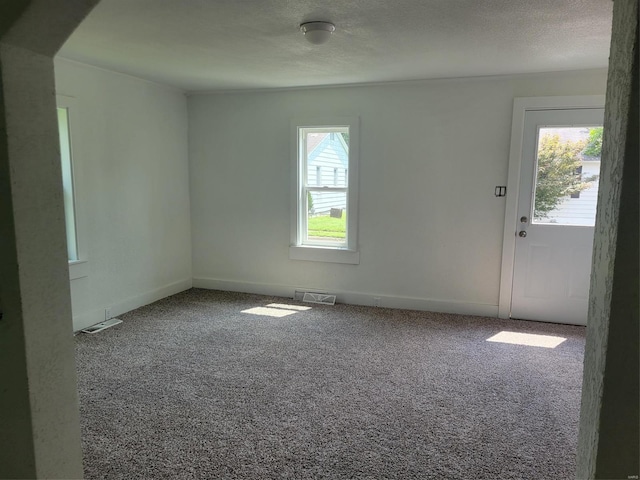 unfurnished room with carpet floors, baseboards, visible vents, and a textured ceiling