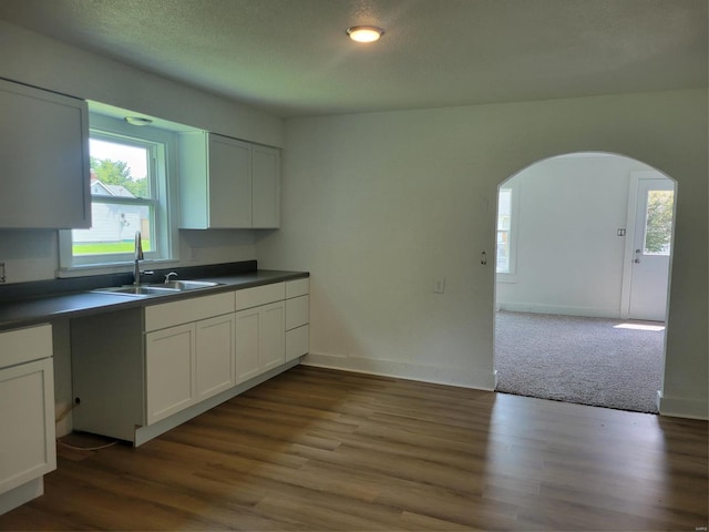 kitchen with arched walkways, white cabinets, a sink, and dark countertops