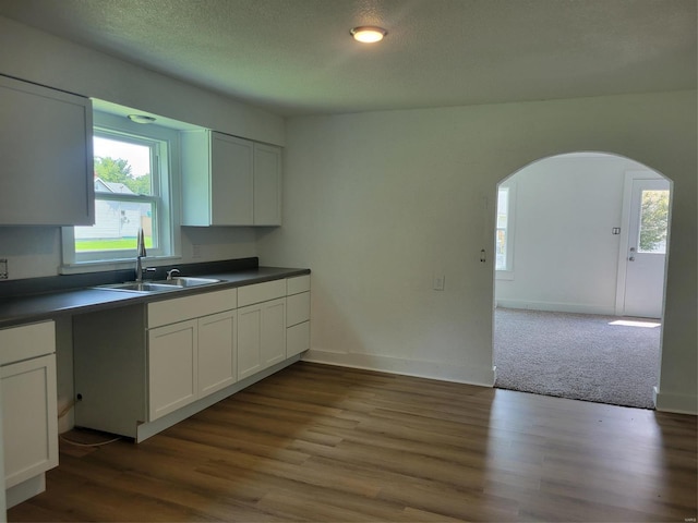 kitchen with dark countertops, white cabinetry, a sink, and arched walkways