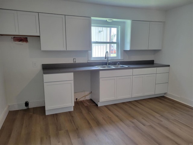 kitchen featuring baseboards, a sink, white cabinetry, and light wood-style floors