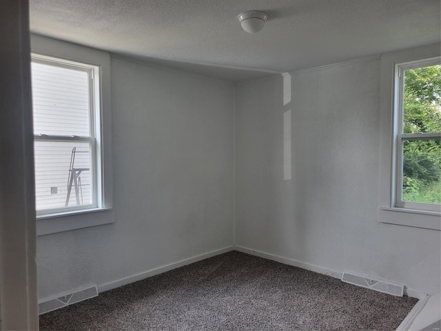 unfurnished room featuring dark colored carpet, a healthy amount of sunlight, visible vents, and a textured ceiling