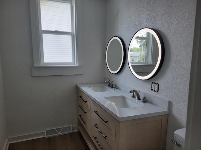 bathroom with double vanity, visible vents, a sink, and wood finished floors