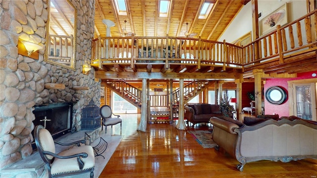 living room featuring wood ceiling, hardwood / wood-style floors, high vaulted ceiling, a skylight, and a stone fireplace