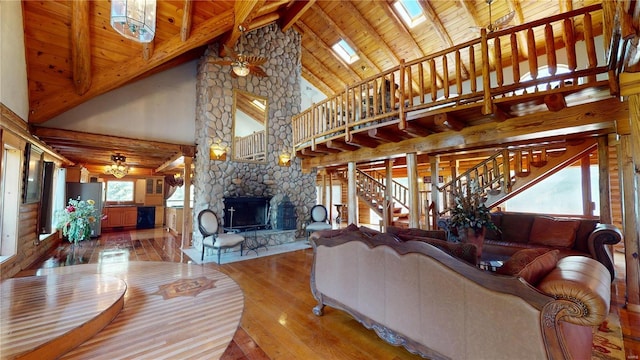 living room with hardwood / wood-style flooring, high vaulted ceiling, beamed ceiling, a skylight, and a stone fireplace