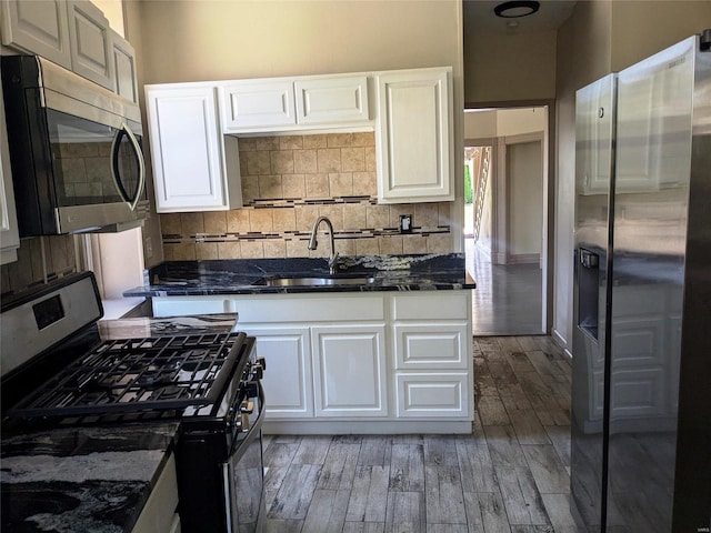 kitchen with appliances with stainless steel finishes, white cabinets, wood-type flooring, and dark stone counters