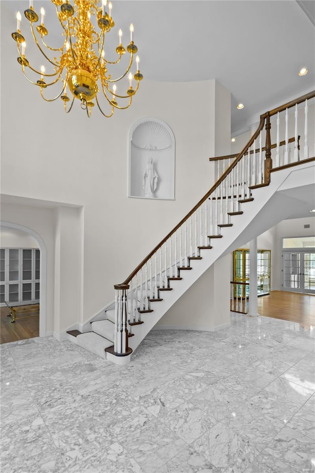 stairway with a towering ceiling, wood-type flooring, and a chandelier