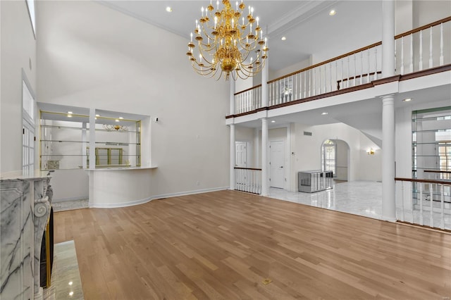 unfurnished living room featuring beam ceiling, ornate columns, a notable chandelier, hardwood / wood-style flooring, and a towering ceiling