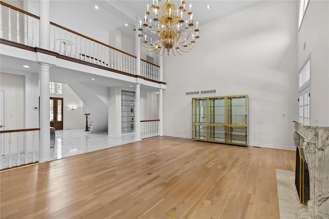 unfurnished living room featuring a chandelier, a high ceiling, ornate columns, light hardwood / wood-style floors, and a fireplace