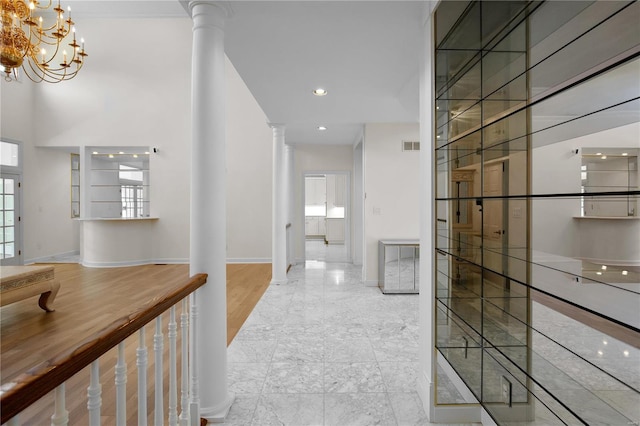 corridor with a notable chandelier, light hardwood / wood-style floors, and ornate columns