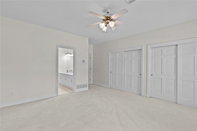 unfurnished bedroom featuring ceiling fan, two closets, connected bathroom, and light carpet