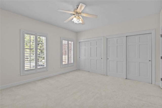 unfurnished bedroom with ceiling fan, two closets, and light carpet