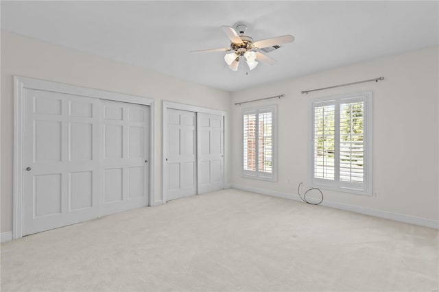 unfurnished bedroom featuring ceiling fan, light carpet, and multiple closets