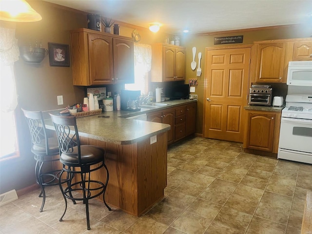 kitchen featuring white appliances, visible vents, dark countertops, a kitchen bar, and a sink