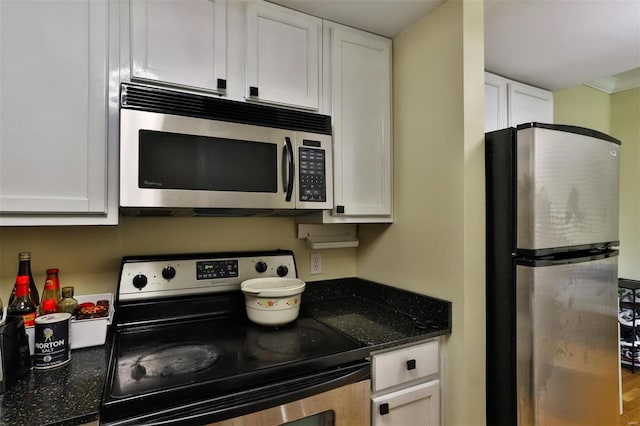 kitchen with white cabinets, dark stone countertops, appliances with stainless steel finishes, and hardwood / wood-style floors