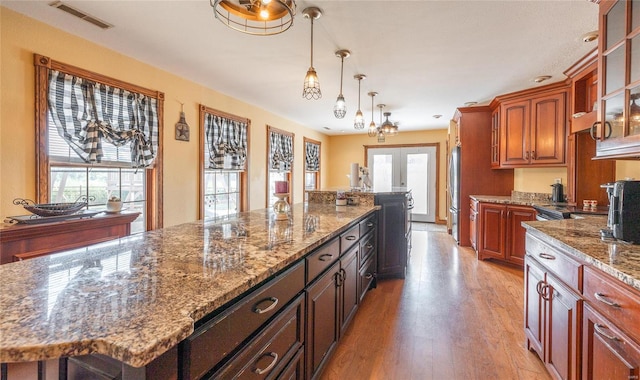 kitchen with light wood-type flooring, stone counters, french doors, a kitchen island, and hanging light fixtures