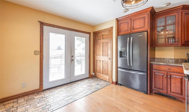 kitchen with stone counters, light hardwood / wood-style floors, a healthy amount of sunlight, and stainless steel refrigerator with ice dispenser