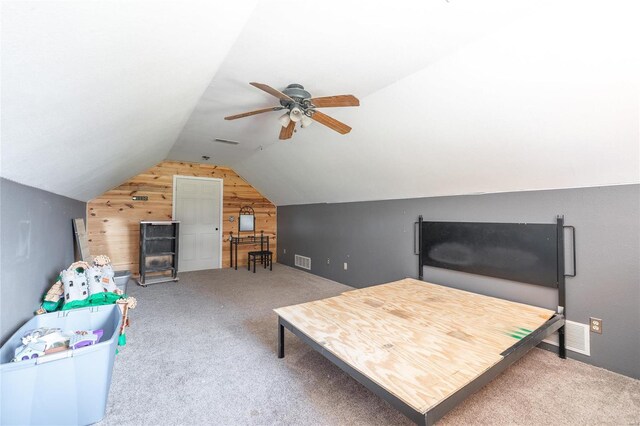 interior space featuring carpet floors, vaulted ceiling, ceiling fan, and wooden walls