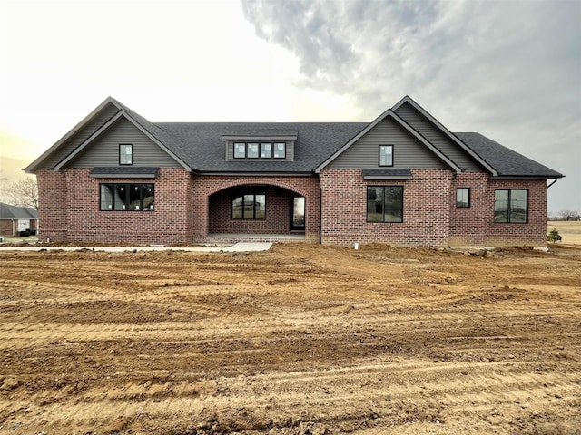 view of front of property with a shingled roof and brick siding