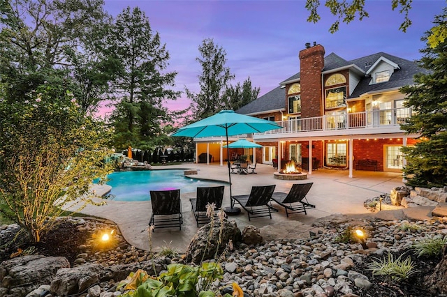 pool at dusk featuring an outdoor fire pit and a patio