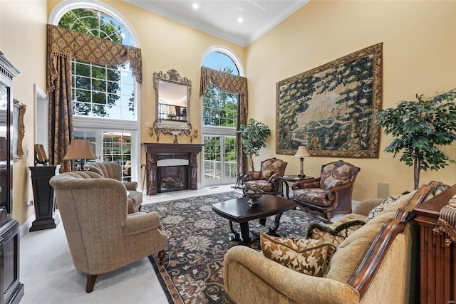 carpeted living room featuring a fireplace, a wealth of natural light, a towering ceiling, and ornamental molding