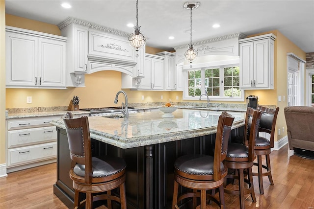 kitchen featuring pendant lighting, a breakfast bar, sink, an island with sink, and light stone counters