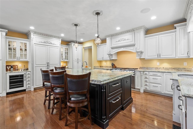 kitchen with hanging light fixtures, wine cooler, white cabinets, and a center island with sink