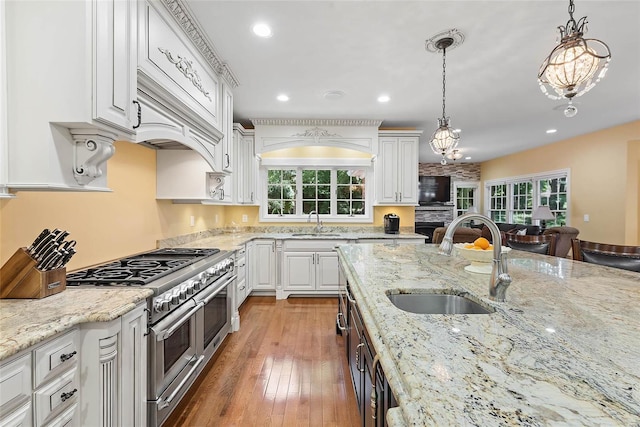 kitchen with double oven range, white cabinetry, decorative light fixtures, light stone countertops, and sink