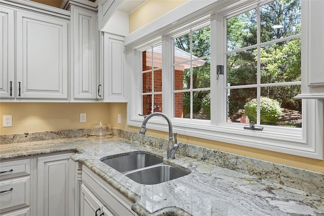 kitchen with white cabinetry, light stone counters, and sink