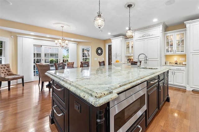 kitchen with stainless steel microwave, pendant lighting, white cabinets, and a kitchen island with sink