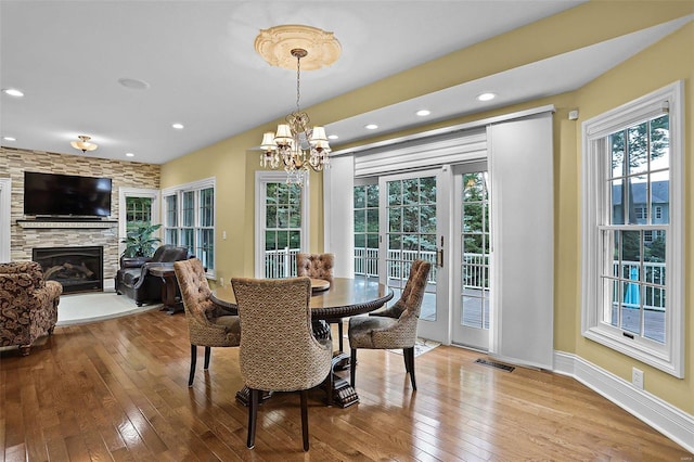 dining area with a stone fireplace, an inviting chandelier, and hardwood / wood-style floors