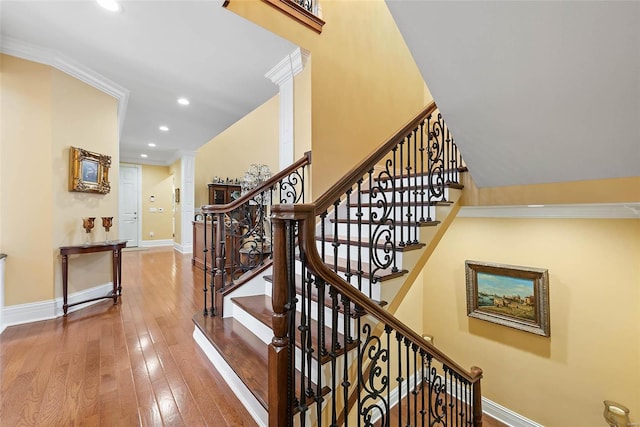 stairway featuring wood-type flooring, ornamental molding, and decorative columns