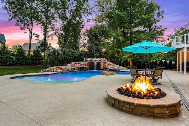 pool at dusk featuring pool water feature, a patio area, and a fire pit