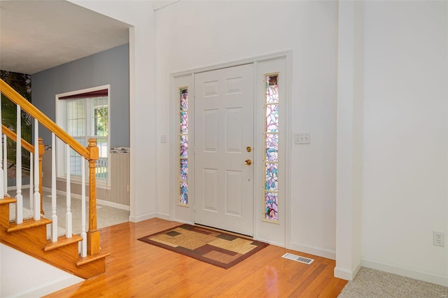 foyer entrance with light wood finished floors, visible vents, stairway, and baseboards