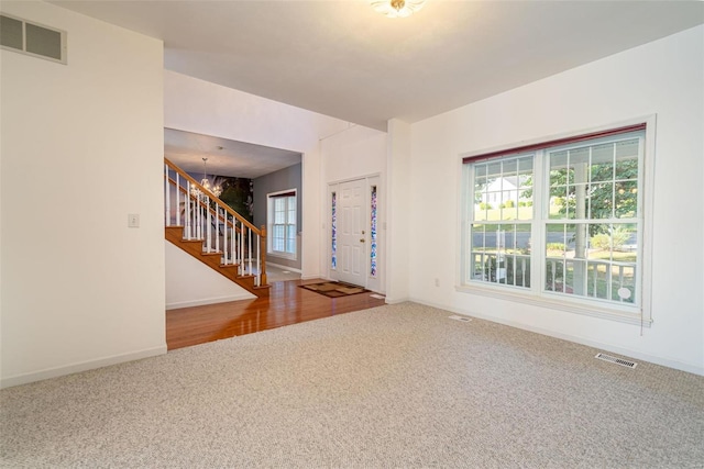 foyer featuring visible vents, a notable chandelier, carpet flooring, and stairs