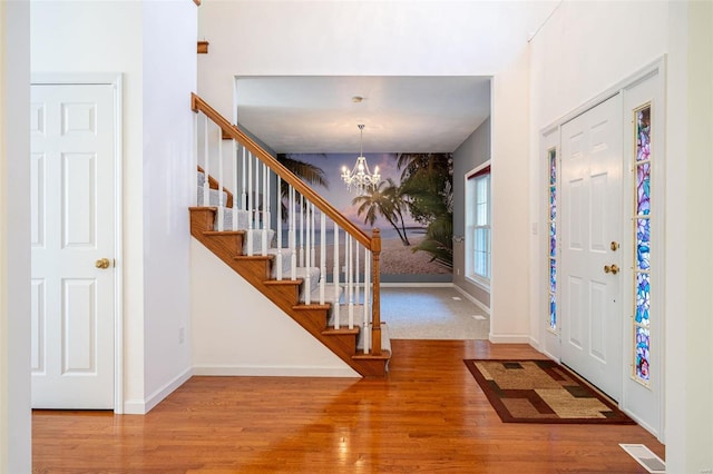 entrance foyer with wood finished floors, baseboards, visible vents, stairs, and a chandelier