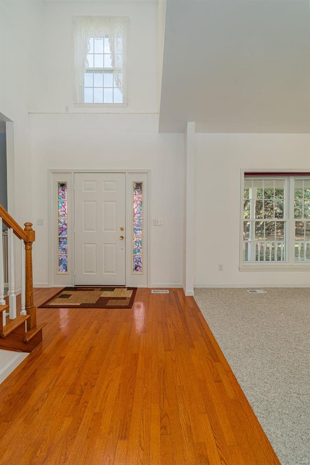 entrance foyer with stairway, baseboards, light wood finished floors, visible vents, and a towering ceiling