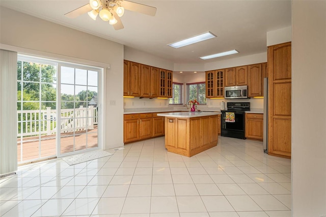 kitchen featuring brown cabinets, stainless steel microwave, black / electric stove, light countertops, and glass insert cabinets