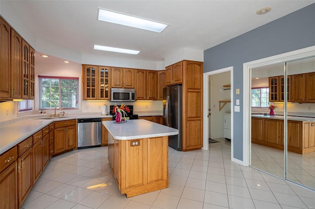 kitchen featuring a sink, glass insert cabinets, appliances with stainless steel finishes, brown cabinets, and a center island